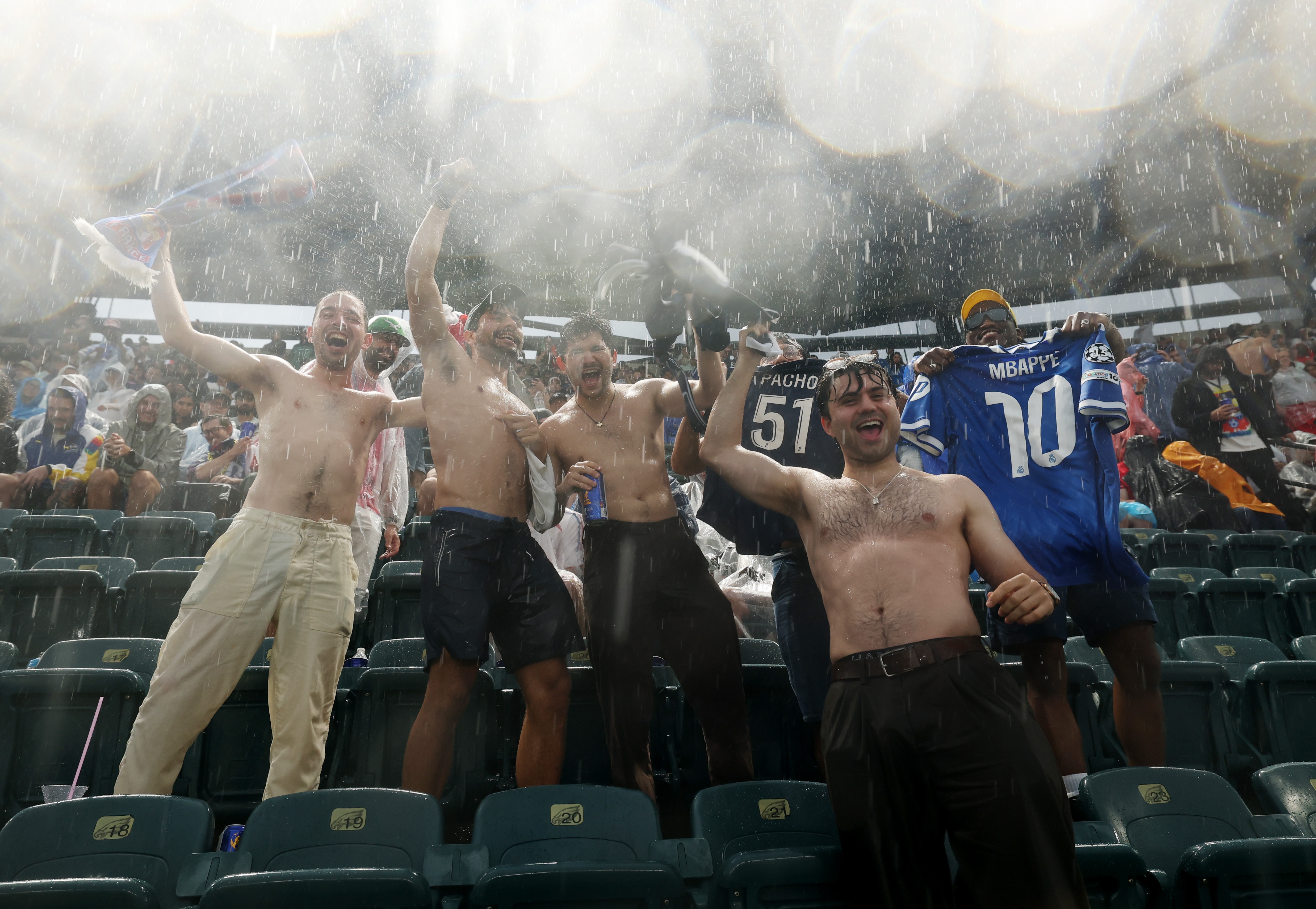 A group of men with no shirts on celebrate in the rain.