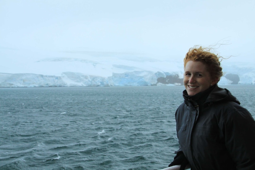 A women, Ceridwen Fraser, stands on a boat with ocean and ice behind her in Antarctica