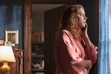 Film still of Amy Adams as Anna dressed in a pink kimono looking out the window, biting her nails in The Woman in the Window