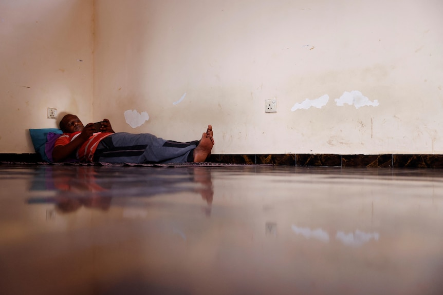 a man lays down on the floor in the corner of a room barefoot