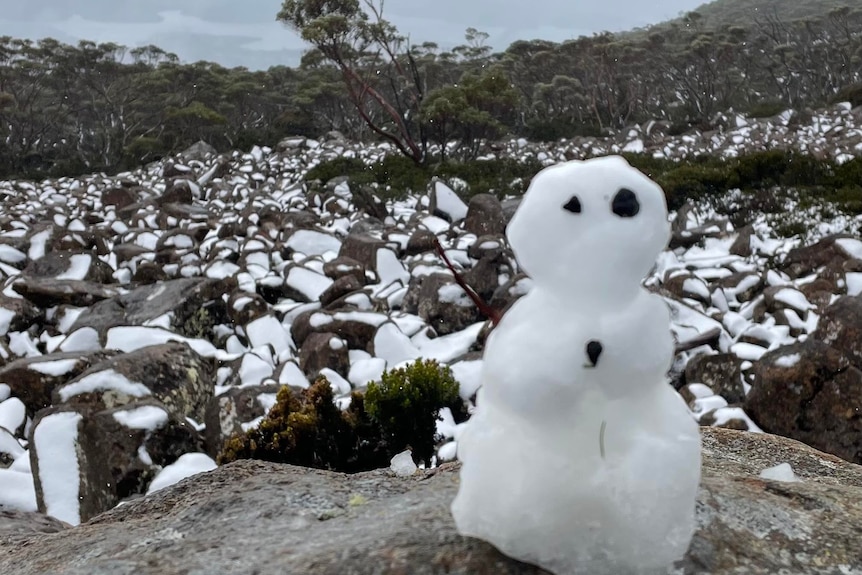 A snowman in front of snow covered boulders.