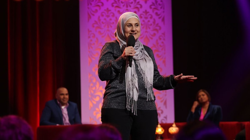 Woman wearing a hijab on stage with a microphone