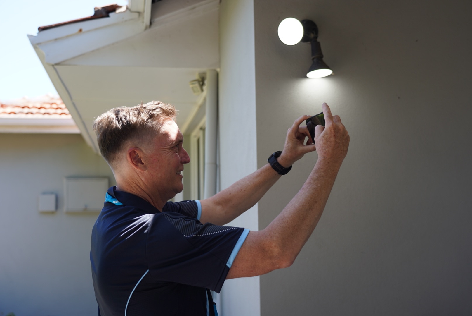 A man fiddles with an electric light outside someone's home. 