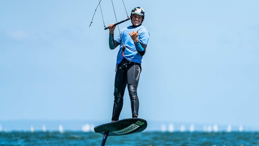 Ocean scene, man standing on kite foil board wearing wetsuit, helmet with bar control in hands for kite surfing