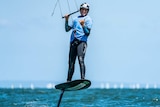 Ocean scene, man standing on kite foil board wearing wetsuit, helmet with bar control in hands for kite surfing