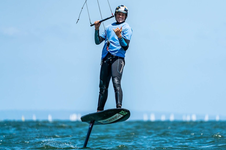 Ocean scene, man standing on kite foil board wearing wetsuit, helmet with bar control in hands for kite surfing