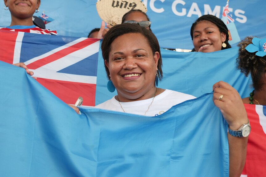 A smiling woman proudly holds the Fijian flag.
