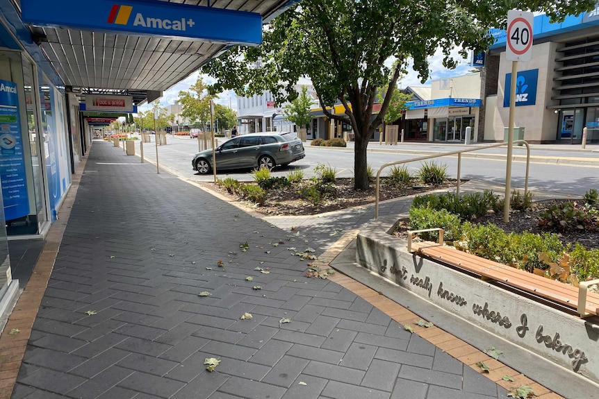 The main street of a town is visible. There are no people and only two cars, one parked, one moving.