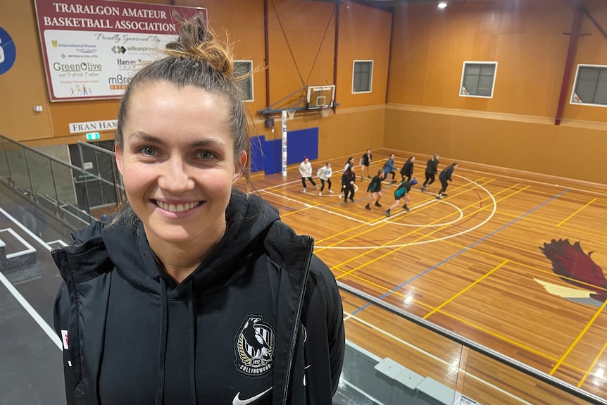 Young woman in Collingwood tracksuit with netball court in the background 