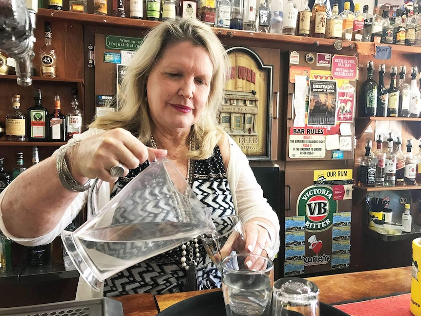 Lady behind a pub counter pours water from a jug into glasses.