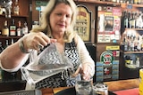 Lady behind a pub counter pours water from a jug into glasses.