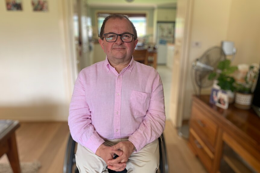 A middle-aged man sitting in a wheelchair. He's wearing glasses and a pink shirt. 