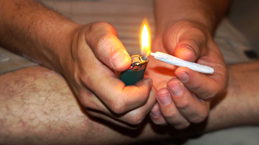 A man sits on the ground and lights a joint.