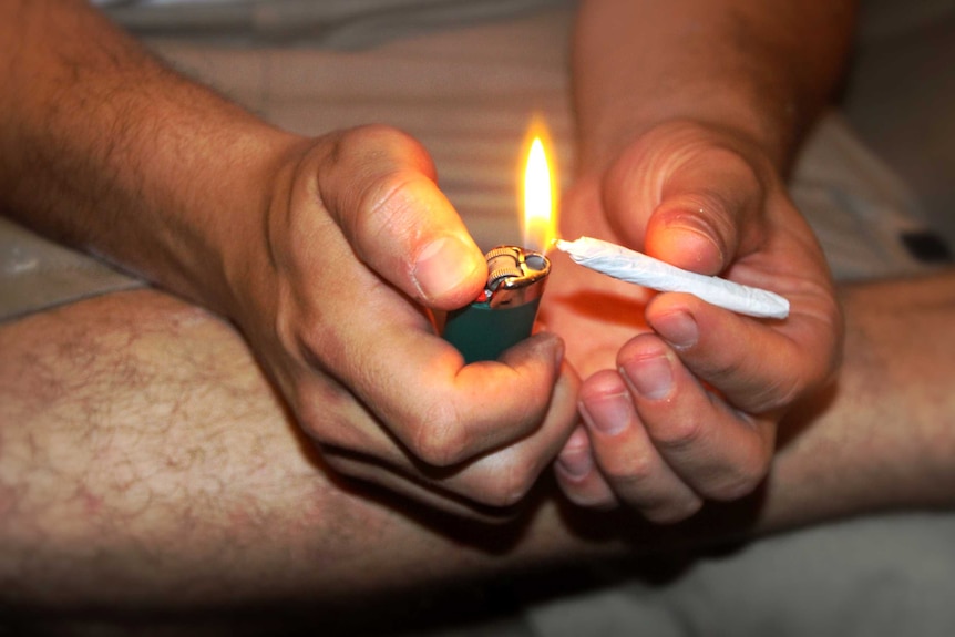 A man sits on the ground and lights a joint.