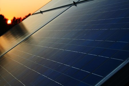 Solar panels on a roof as the sun rises in the background.