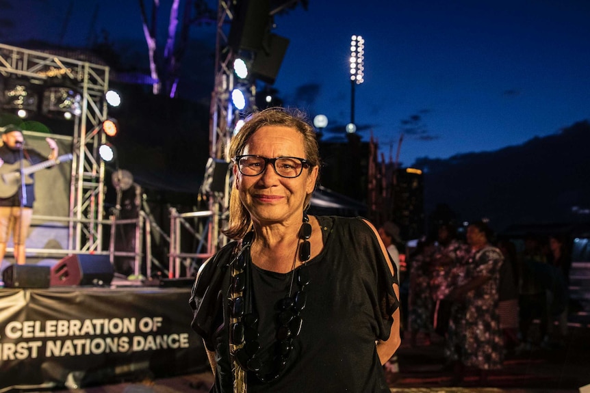 Colour photo of Rhoda Roberts AO standing in front of Dance Rites 2018 stage in the evening.