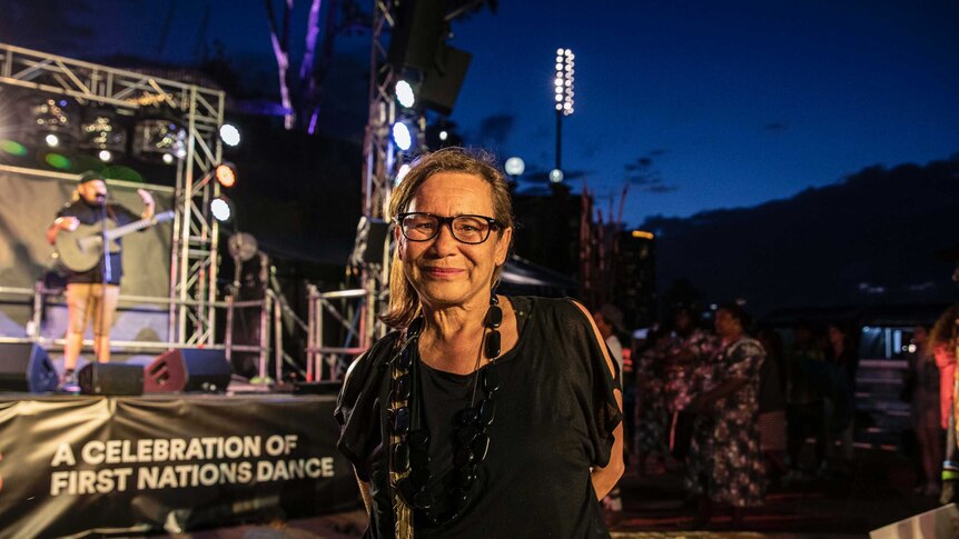 Colour photo of Rhoda Roberts AO standing in front of Dance Rites 2018 stage in the evening.