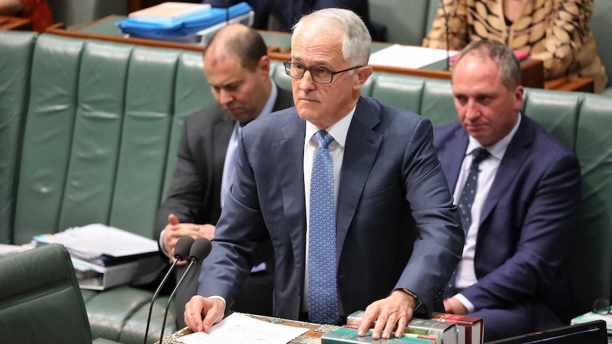 Malcolm Turnbull glares across the room during Question Time. Josh Frydenberg and Barnaby Joyce are behind him looking stern.