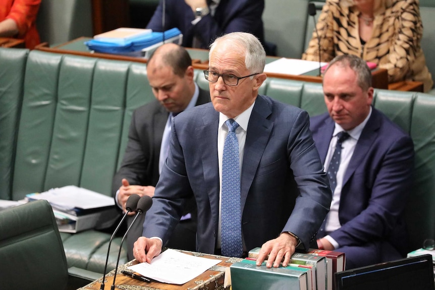 Malcolm Turnbull glares across the room during Question Time. Josh Frydenberg and Barnaby Joyce are behind him looking stern.