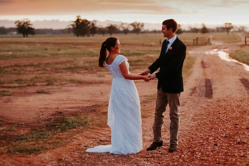 Landscape picture of bride and groom outside against a sunset on their wedding day.