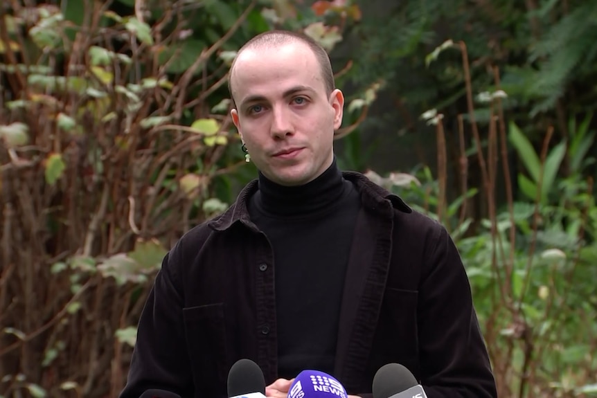 Aiv wearing a black turtleneck standing in front of microphones.