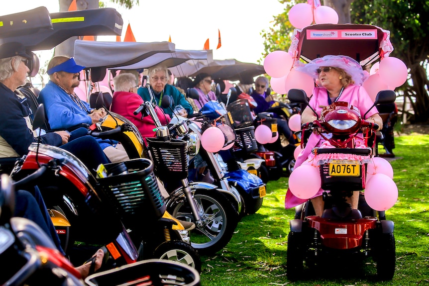 Mobility scooters in a line up with a single scooter dressed in pink.