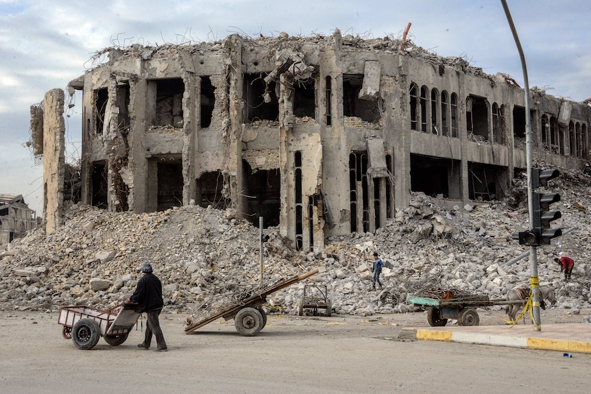 An Iraqi pushes his cart past the rubble of the destroyed seven-storey Chadirji Building.