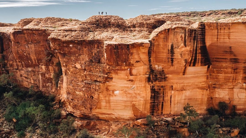 A red cliff face of Kings canyon with people standing on top.