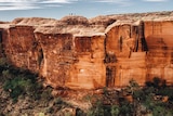 A red cliff face of Kings canyon with people standing on top.