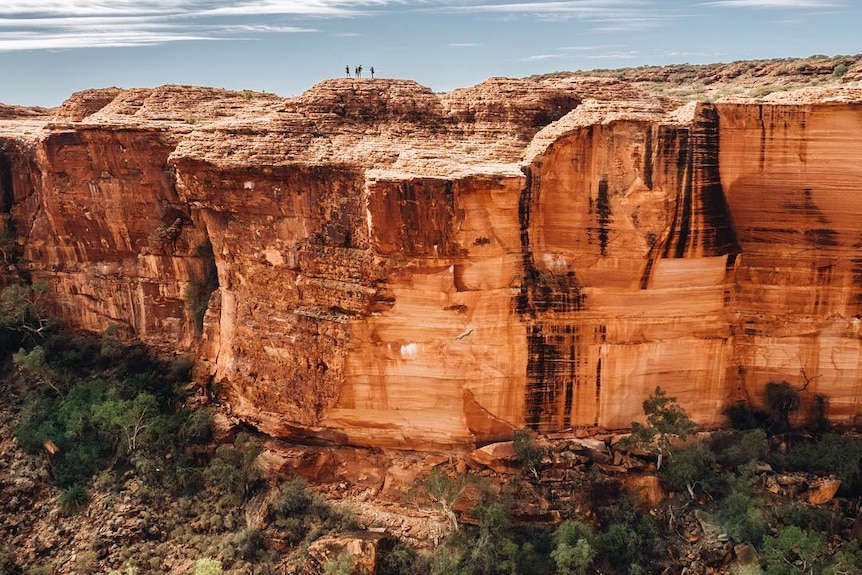 A red cliff face of Kings canyon with people standing on top.