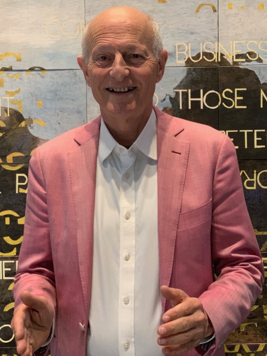 Mature aged man in a pink suit smiles at the camera.