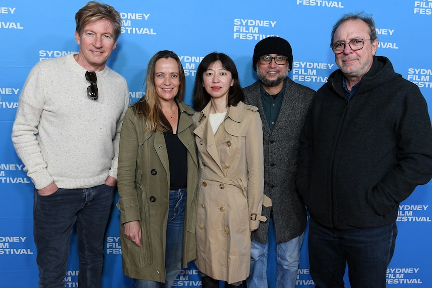 Five men and women standing in a line on a red carpet against a blue photo wall with the logo for Sydney Film Festival.