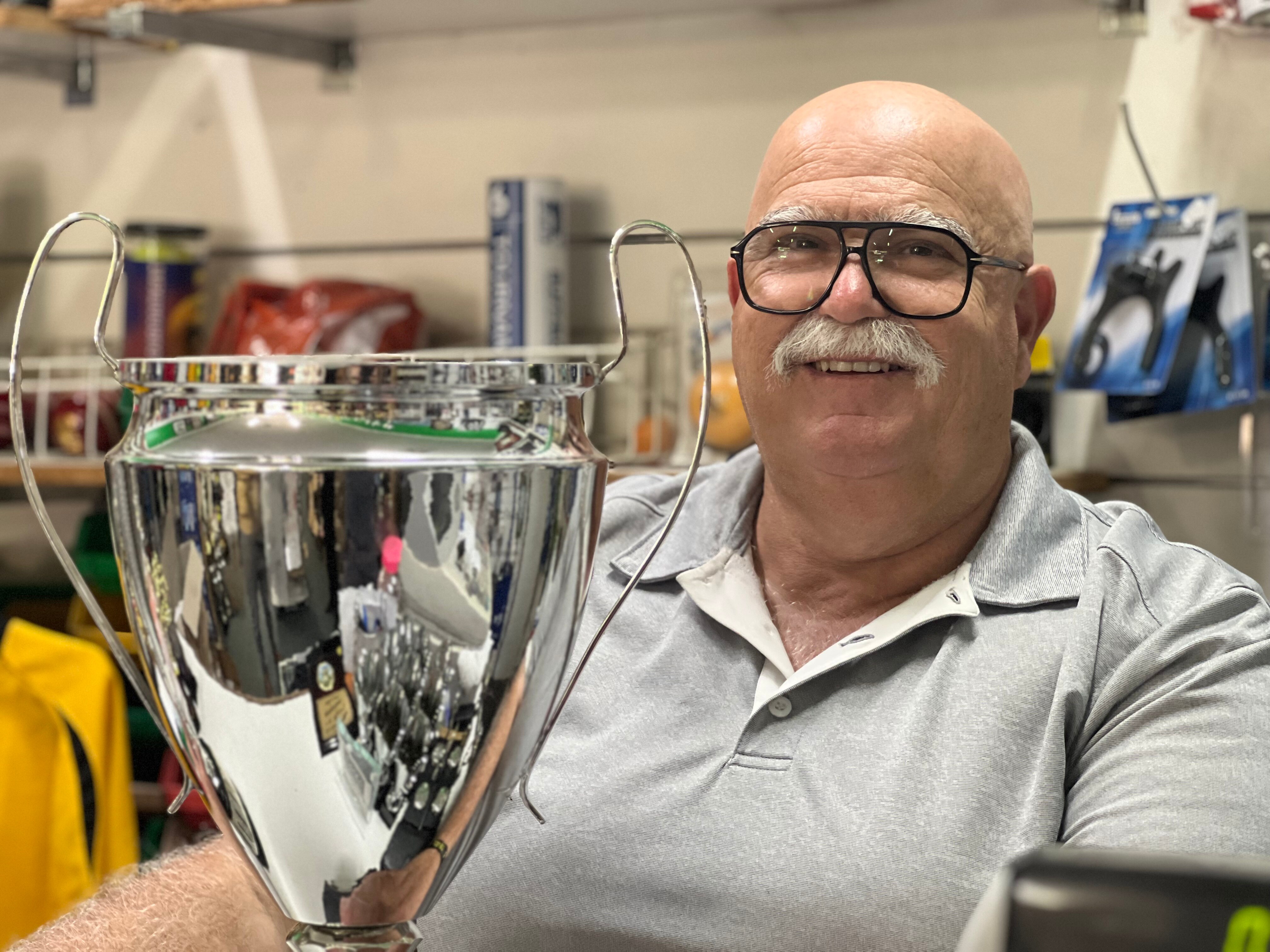 A man sits in front of a large trophy 