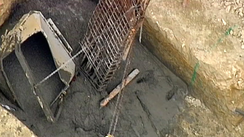 A container lies in a trench full of wet cement after falling from a crane on a construction site.