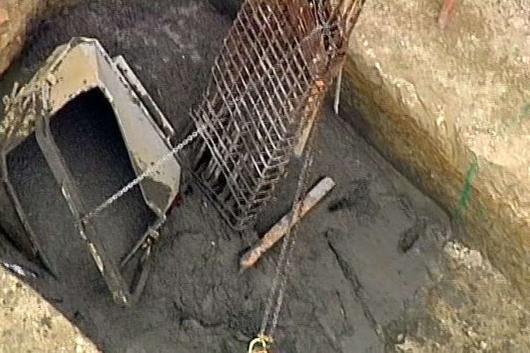 A container lies in a trench full of wet cement after falling from a crane on a construction site.