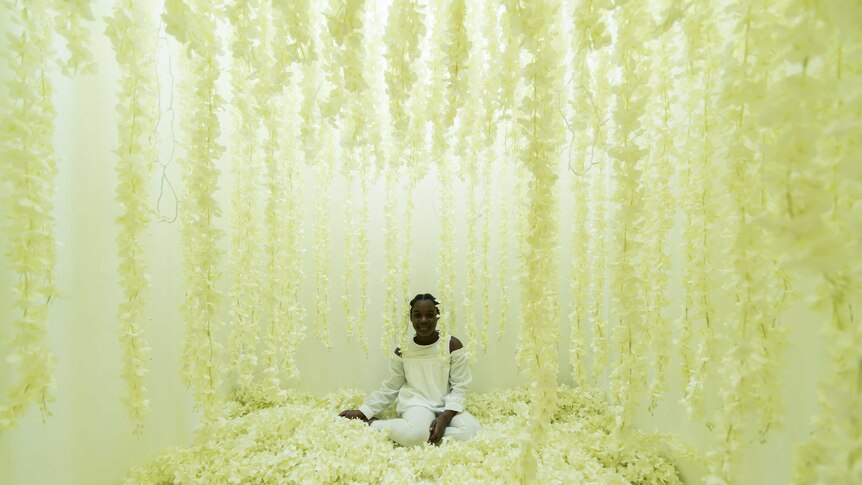 A young girl sits in a room filled with white flowers