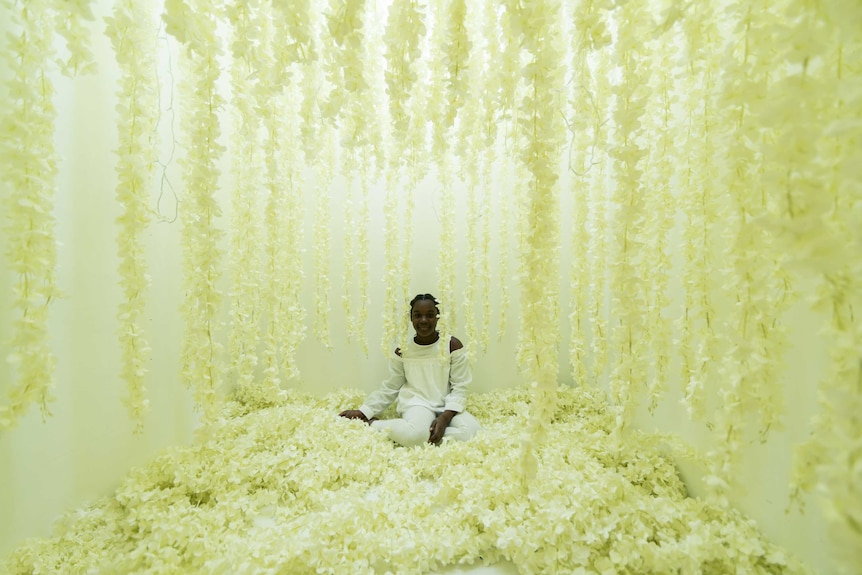 A young girl sits in a room filled with white flowers