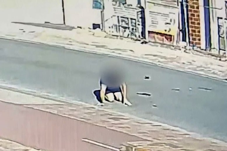 A still image taken from CCTV showing a man hunched over on a road, with his identity blurred.