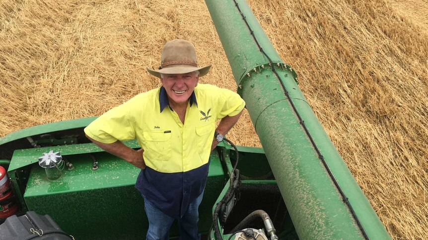 Mallala farmer John Lush stands on machinery in a wheat field looking very happy.