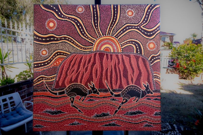 an indigenous painting on an easel showing ayers rock