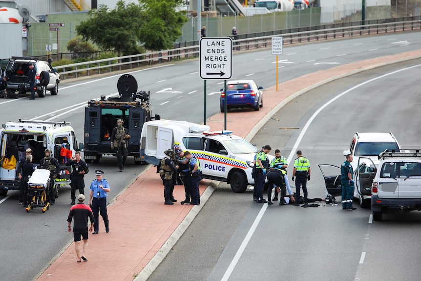 A man lying handcuffed on a road surrounded by police.