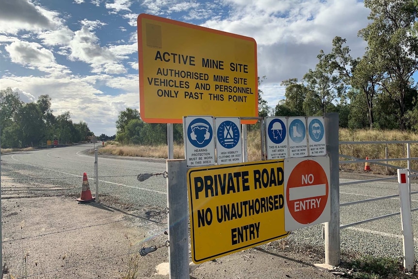 Signs reading 'active mine site' and 'private road — no unauthorised entry' at a gate blocking a road.