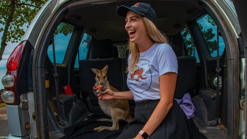 Woman with wallaby in back of car.