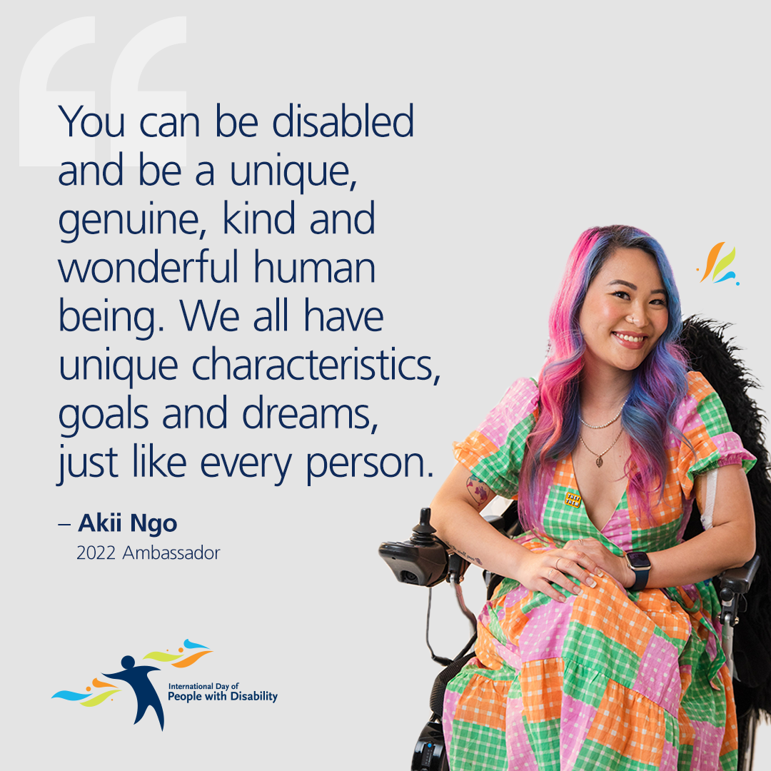 A person with pink and blue hair and a coloured dress sits in a wheelchair next to disability affirming quote.