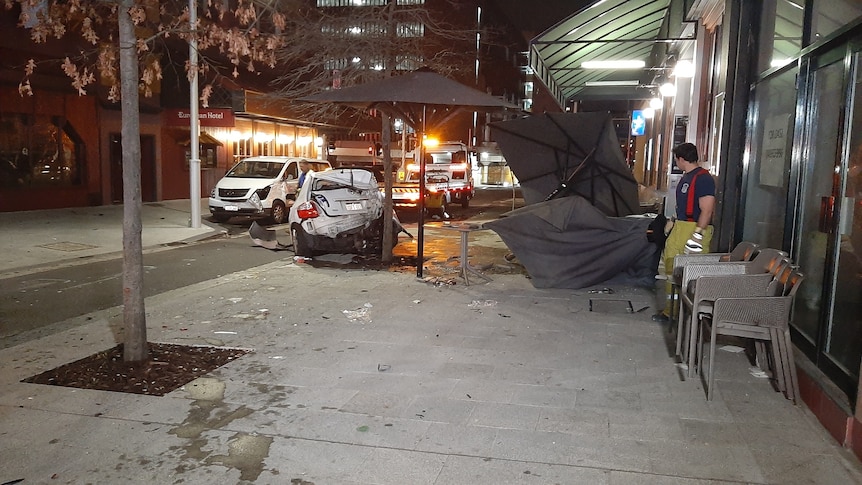 A man in emergency worker uniform looks at a smashed car outside a restaurant.