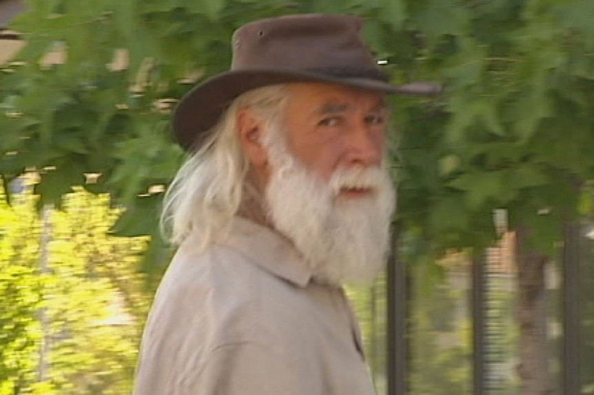 A man with a long white beard and wearing a hat walks towards the ACT Magistrate Court.