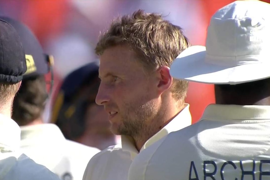 Joe Root stands and looks out, surrounded by teammates