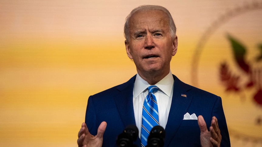 Joe Biden behind a lecturn with a yellow background and the Presidential seal