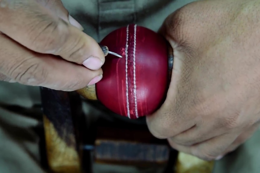 A hand holding a partially sewn together cricket ball.