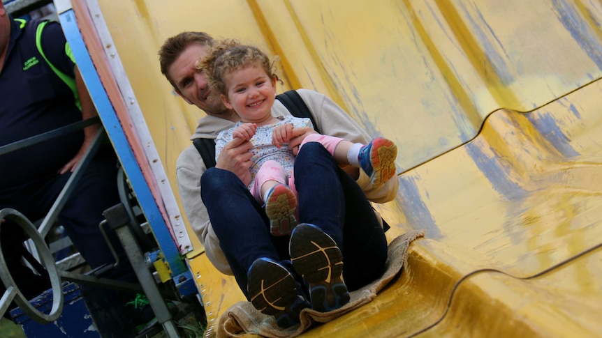 A man and little girl ride a slide.